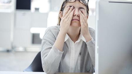 Frau im Büro greift sich auf ihre Augen, die müde sind von der Bildschirmarbeit