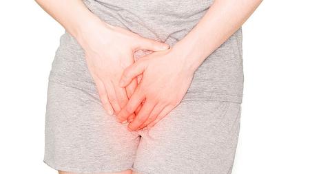 Frau hat wegen bakterieller Vaginose Schmerzen im Unterleib und hält sich den Intimbereich