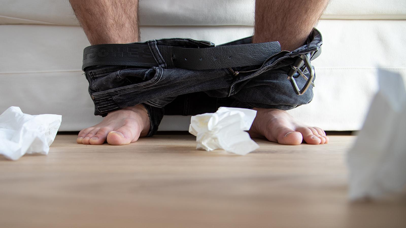 Mann sitzt mit heruntergelassenen Hosen auf einer Couch