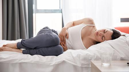 Frau mit Harnwegsinfekt nach dem Sex liegt mit Schmerzen im Bett