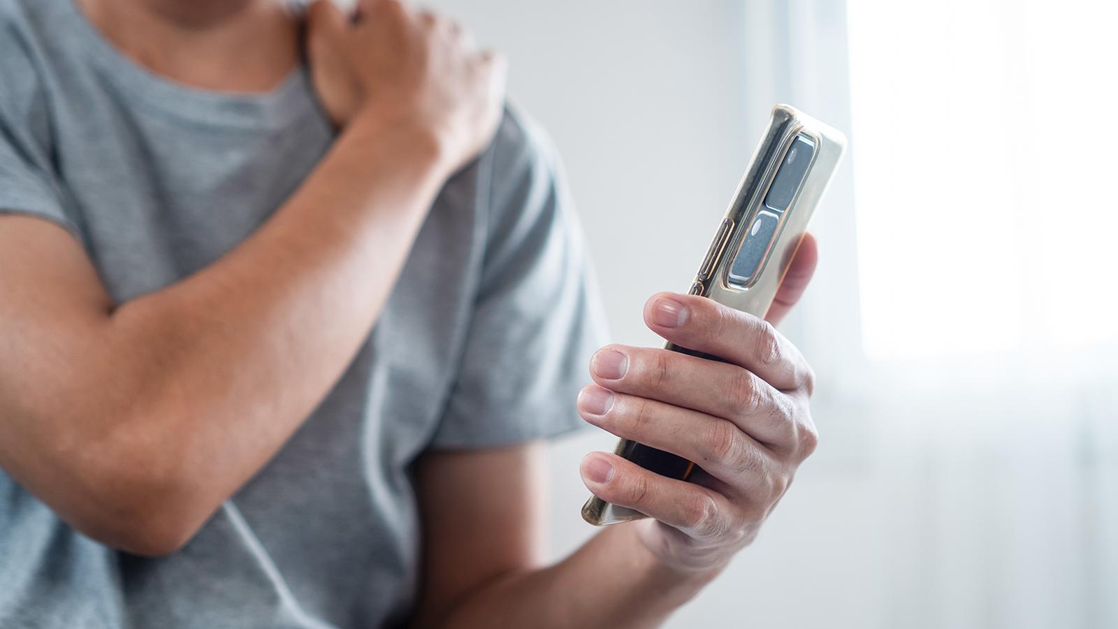 Mann hat Schmerzen in der Schulter, nachdem er sein Handy zu lange in der Hand gehalten hat