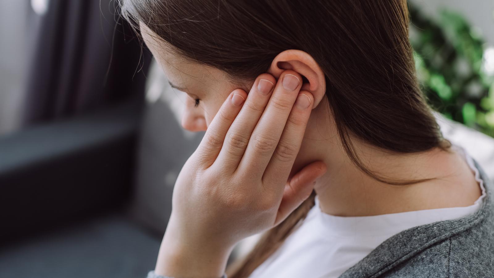 Junge Frau hat durch einen Tinnitus Ohrenschmerzen.