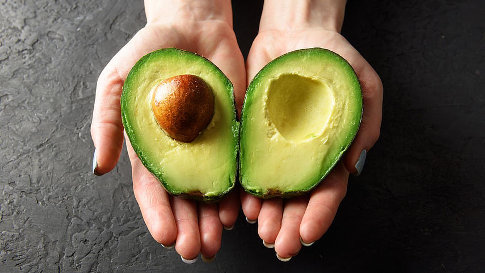 Frau hält aufgeschnittene Avocado in der Hand. 