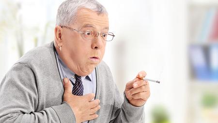 Älterer Mann hustet, während er eine Zigarette raucht