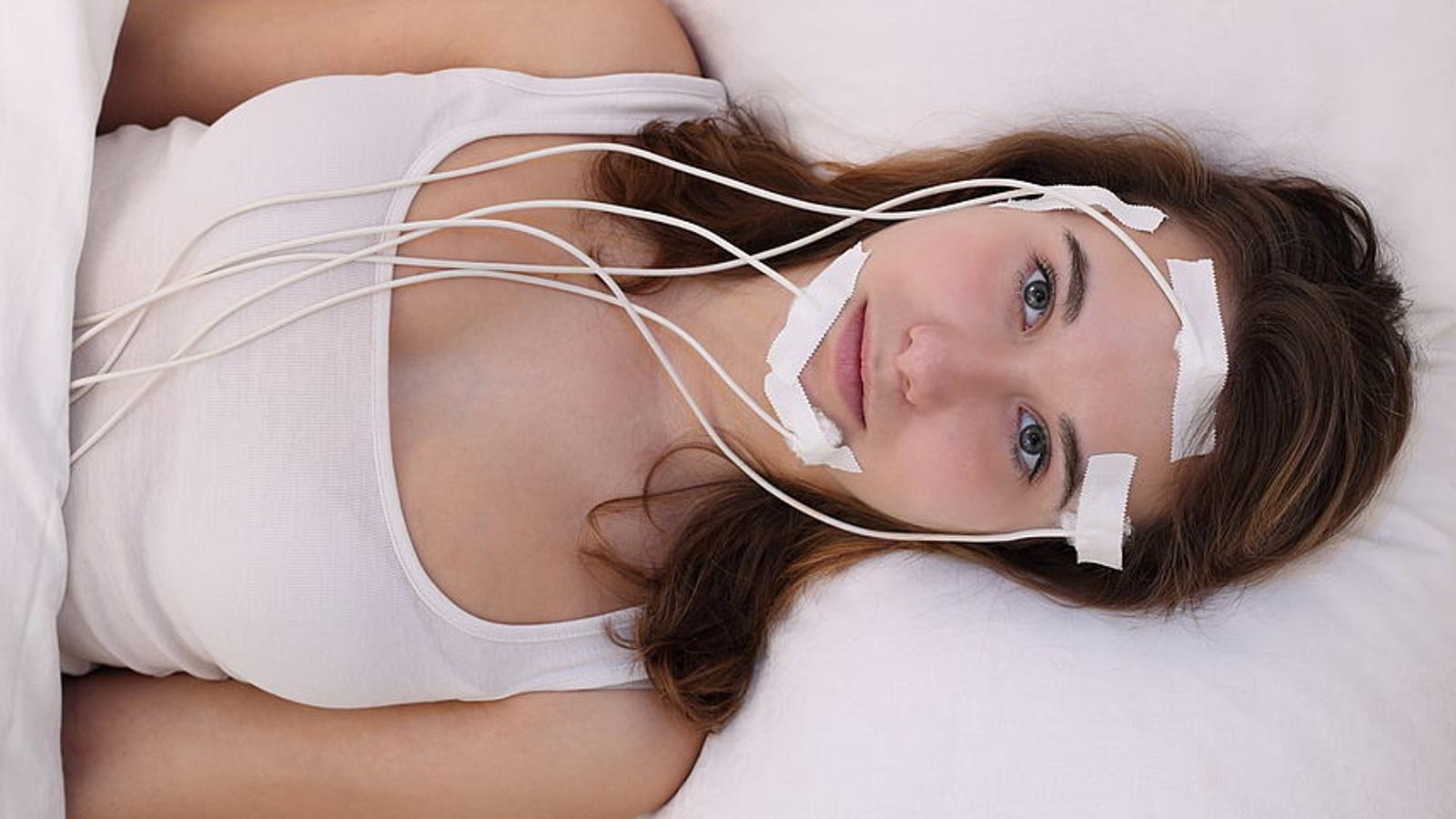 Junge Frau mit Schlafproblemen liegt mit Kabeln im Gesicht im Schlaflabor