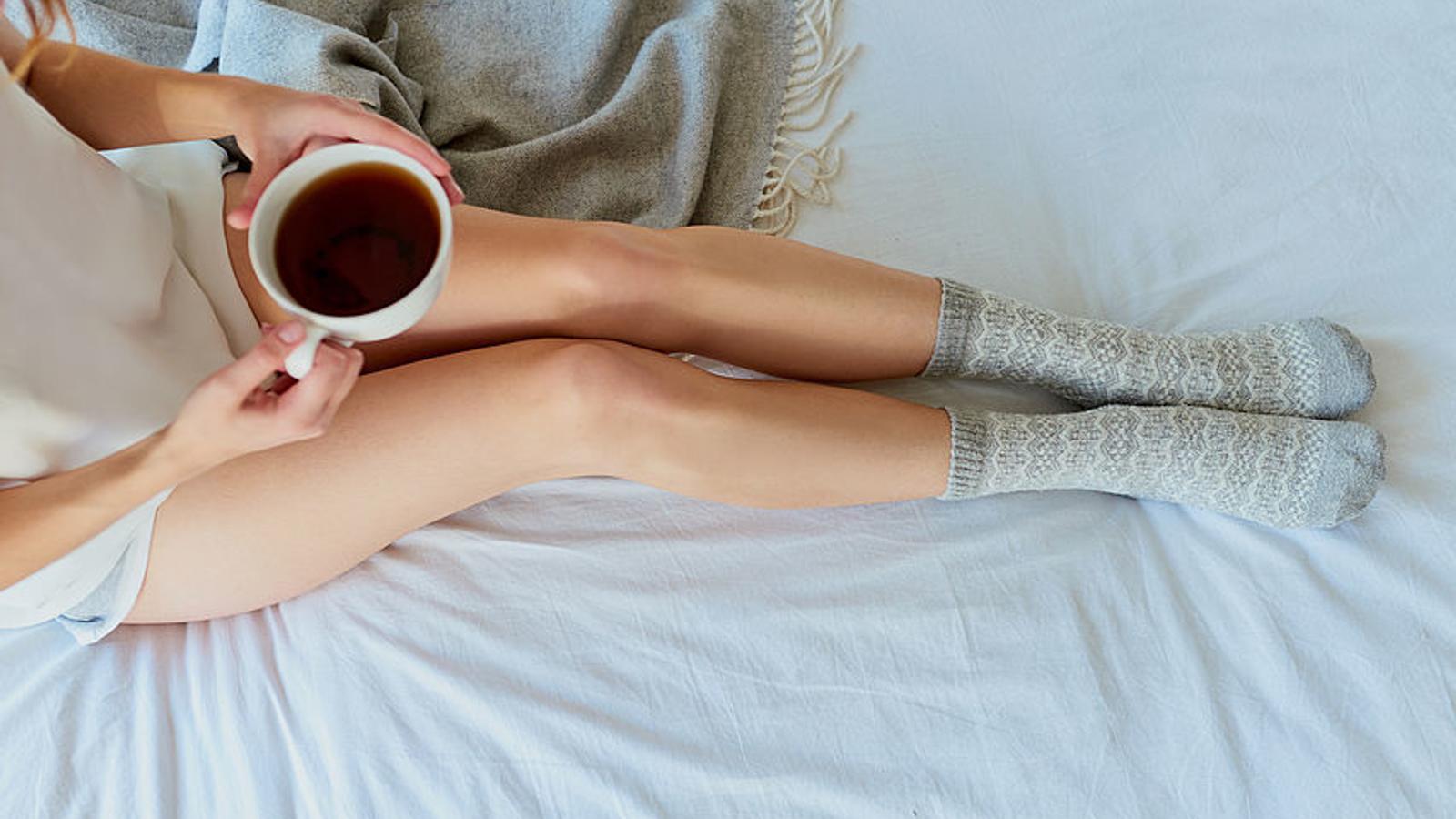 Frau sitzt mit einer Tasse Tee am Bett