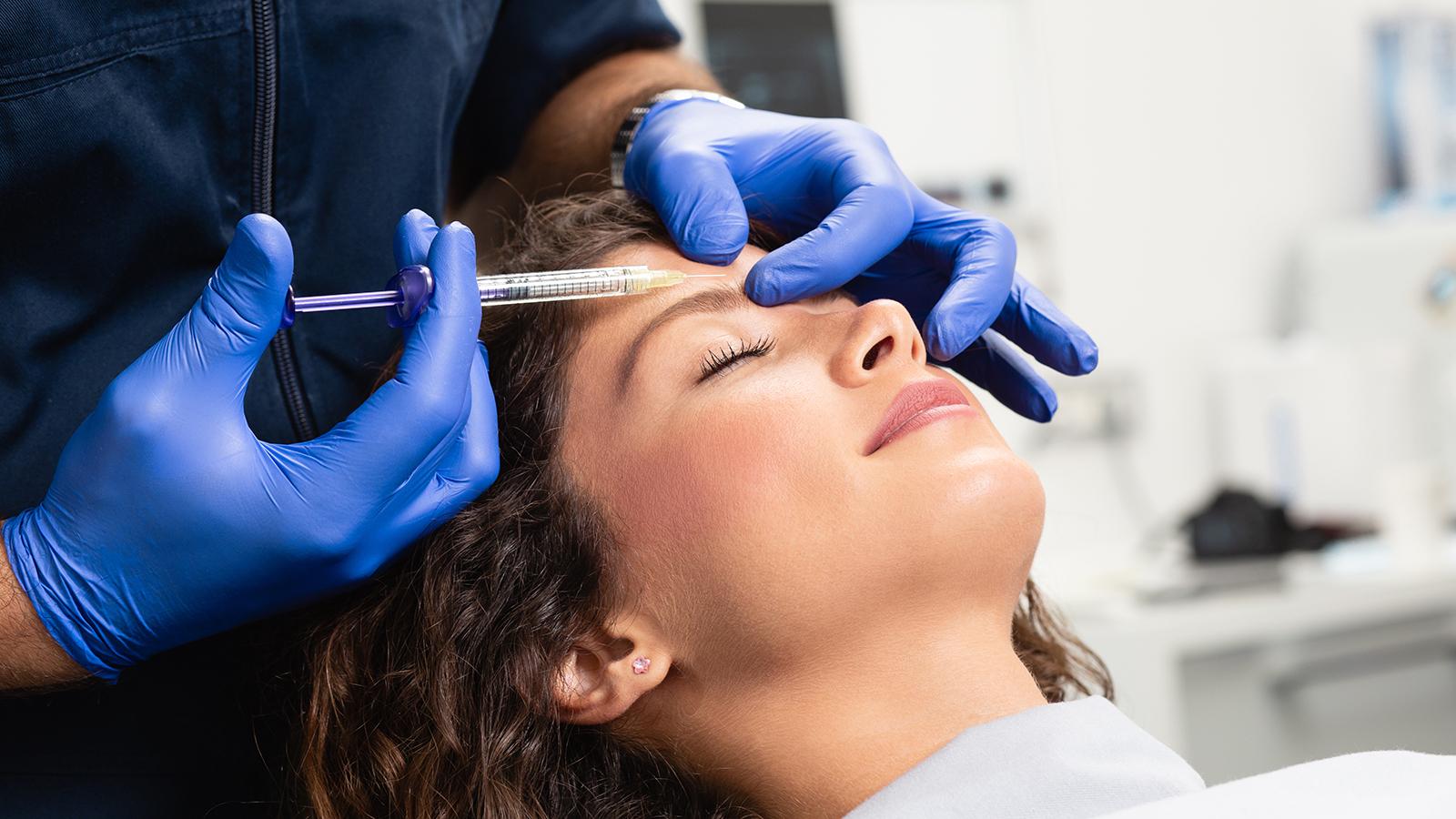 Arzt spritzt Frau Botox in die Stirn