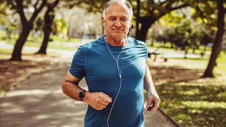 Älterer Mann mit Kopfhörern joggt im Park