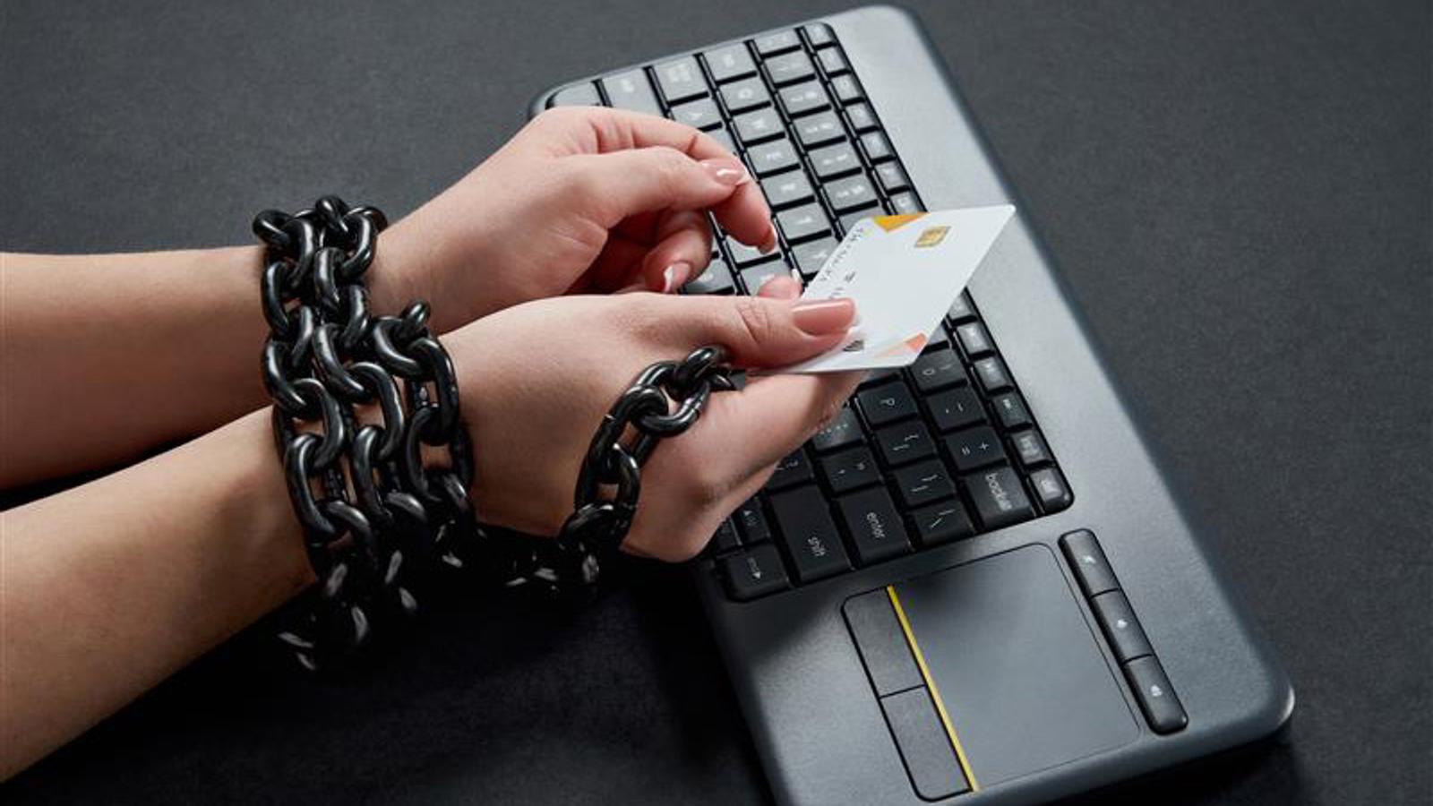 Hände in Ketten gelegt, halten Kreditkarte über Tastatur