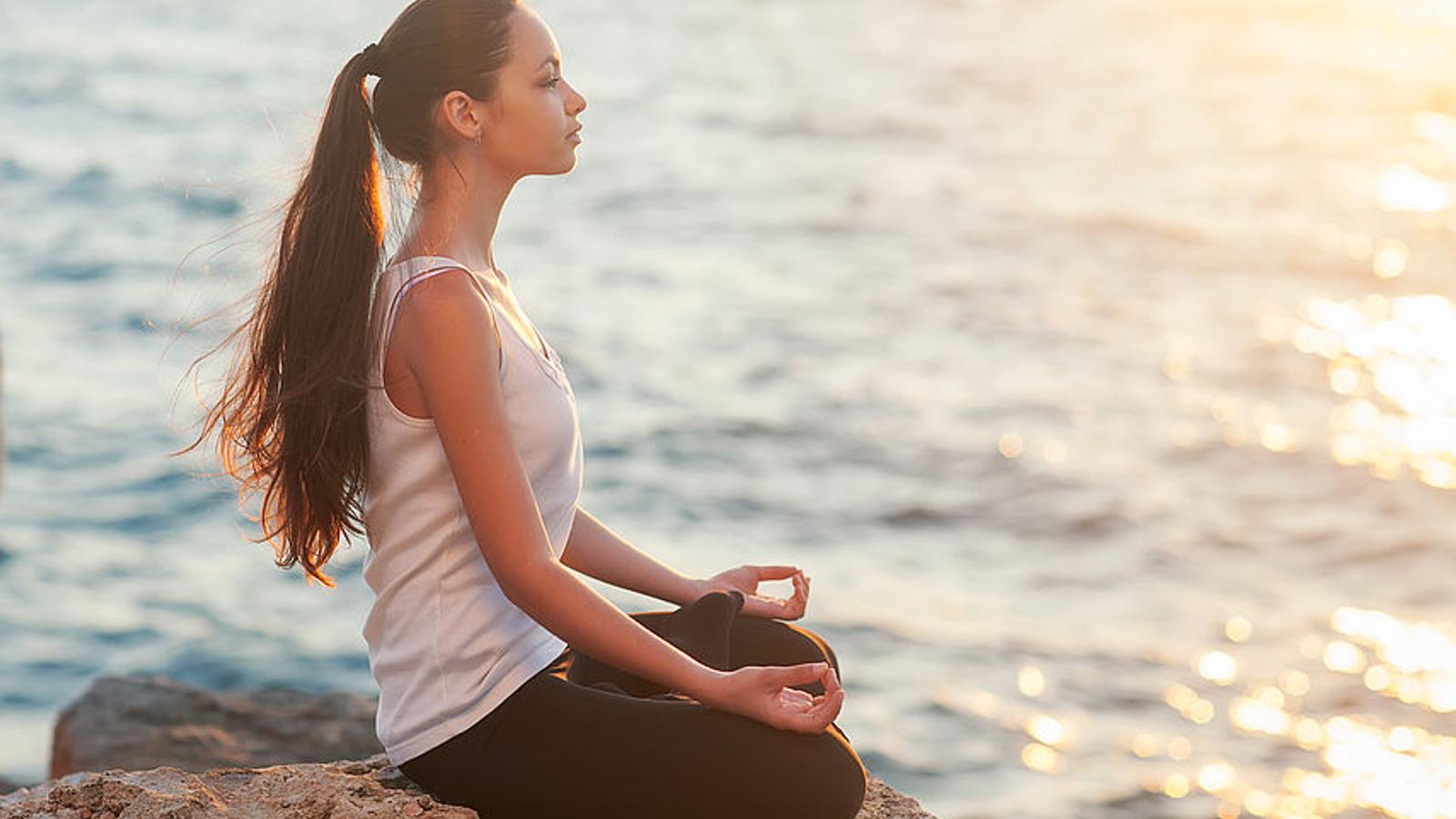 Junge Frau entspannt sich am Meer mit Mediation und Atemübungen