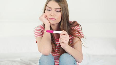 Junge Frau hält enttäuscht einen negativen Schwangerschaftstest in der Hand