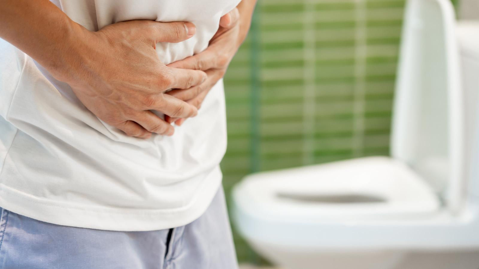 Mann mit Magen-Darm-Grippe auf der Toilette, greift sich auf den Bauch