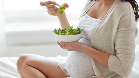 Schwangere Frau isst Salat. 