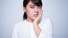 Frau hält sich die Wange vor lauter Zahnschmerzen