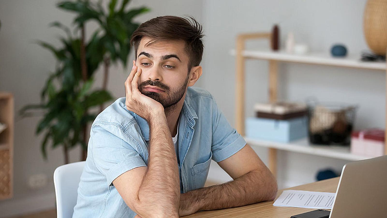 Gelangweilter Mann mit Boreout sitzt am Schreibtisch.