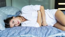 Frau mit Unterleibsschmerzen liegt im Bett