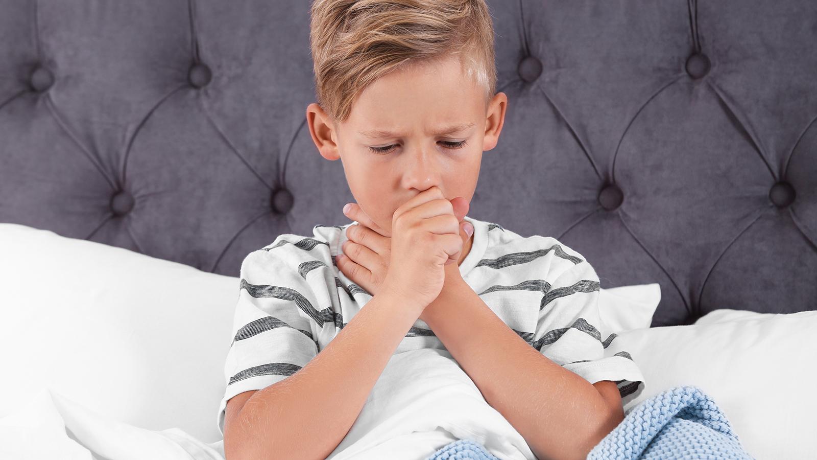 Junge sitzt im Bett, leidet an einer Bronchitis und muss husten. 