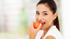 Junge Frau beißt in Apfel, der wegen Säure schlecht für die Zähne ist