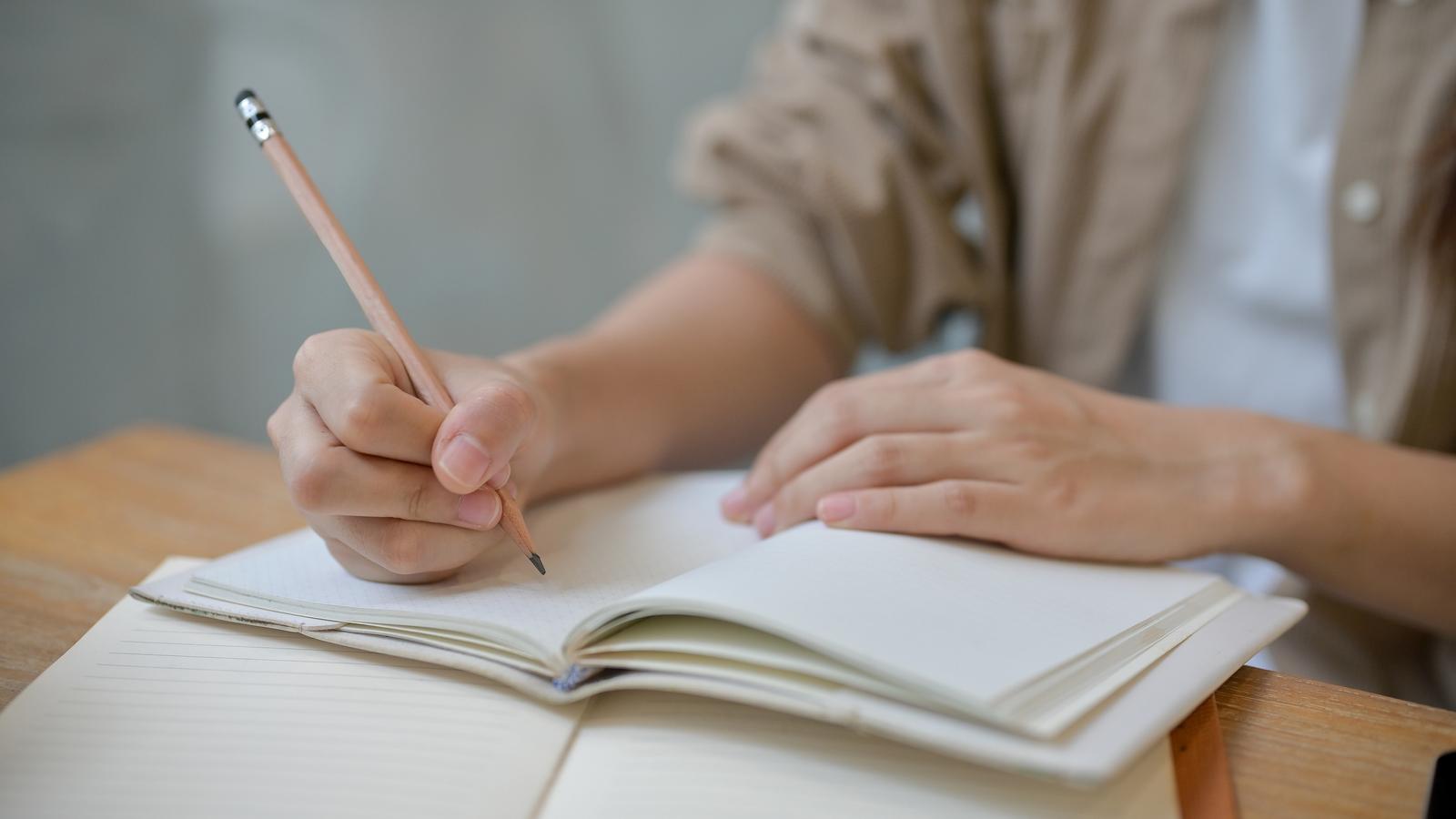 Person schreibt in ein Notizbuch, um die Gedächtnisübungen zu lösen.