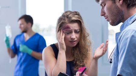 Frau mit Kopfwunde spricht mit Arzt in der Unfallambulanz
