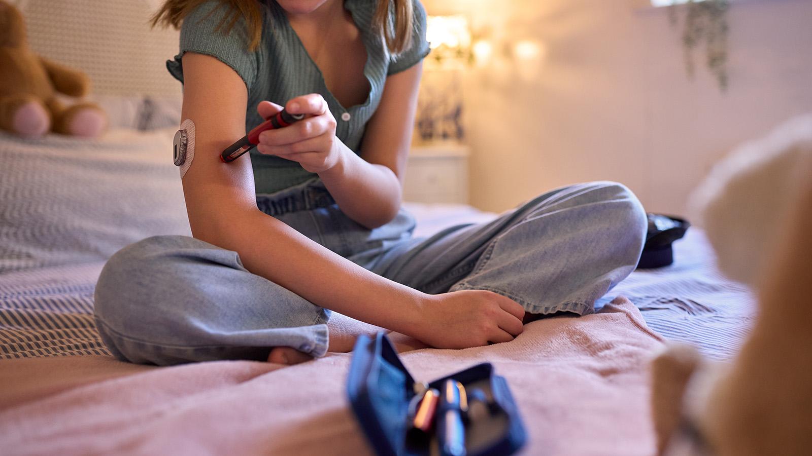 Mädchen sitzt auf ihrem Bett und prüft ihren Insulinspiegel