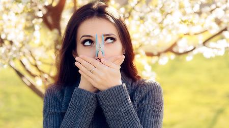 Frau steckt sich wegen einer Pollenallergie eine Kluppe auf die Nase