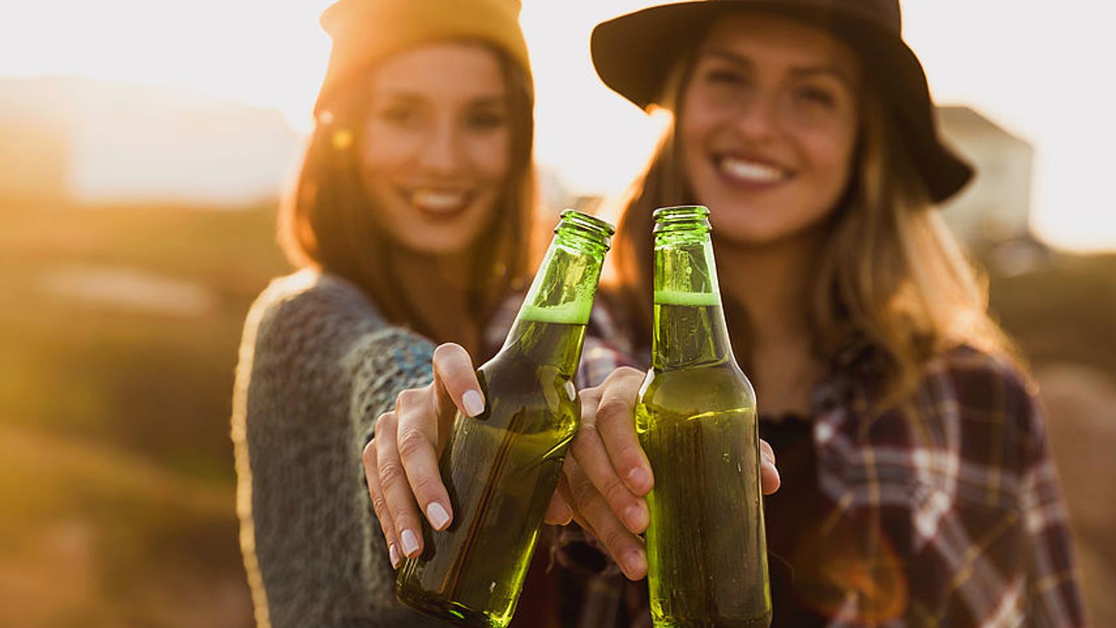 Zwei Frauen stoßen mit einem Bier an.