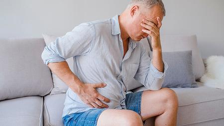 Mann mit Myelofibrose sitzt mit Bauchschmerzen am Sofa