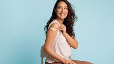 Frau zeigt Pflaster auf der Schulter nach FSME-Impfung