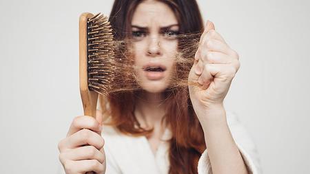 Frau mit Haarverlust zeigt ihre Bürste.