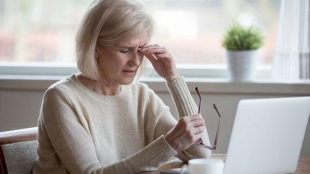 Frau mit Fatigue-Syndrom sitzt vor ihrem Laptop und greift sich wegen starker Müdigkeit müde auf die Augen