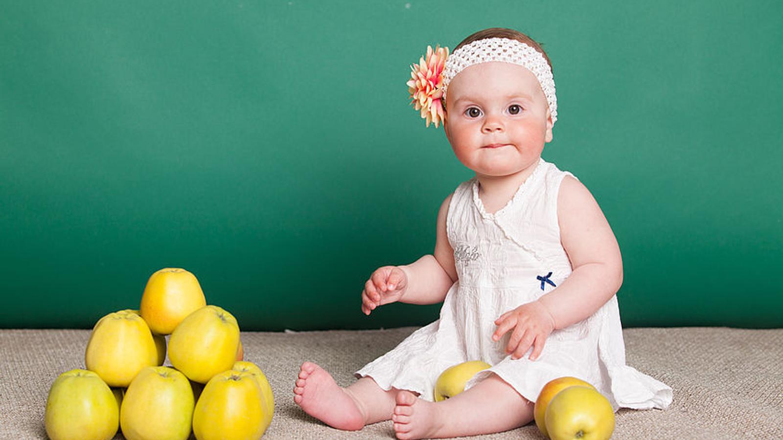 Baby sitzt am Boden und um es herum liegen Äpfel. 