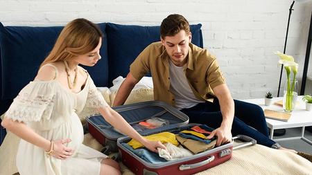 Schwangere Frau packt mit ihrem Partner den Koffer. 