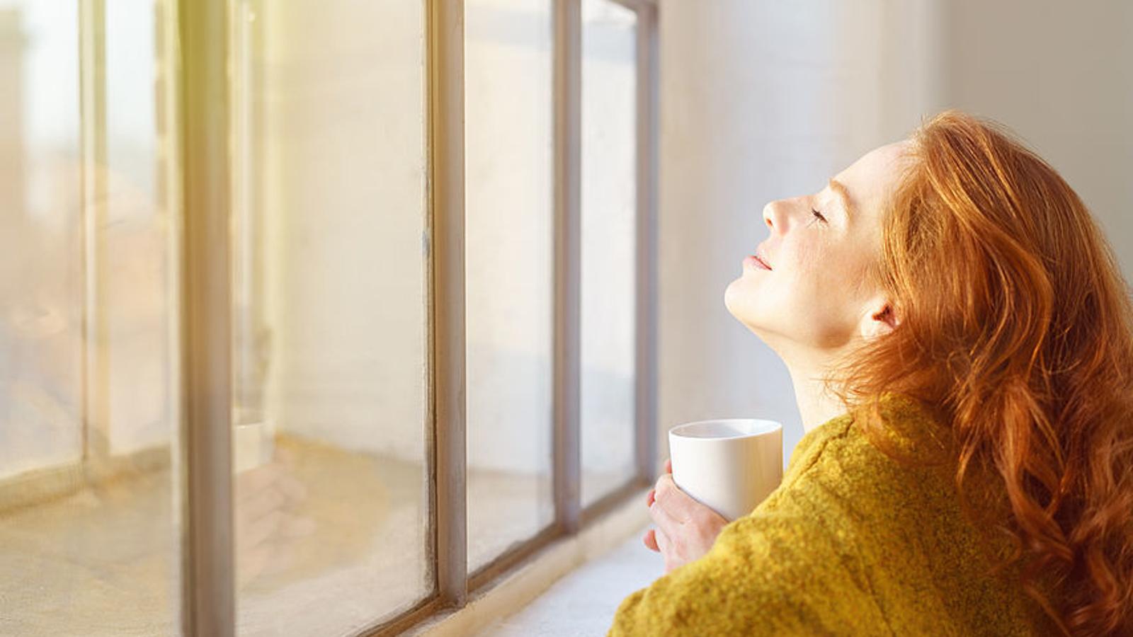 Frau sitzt im Winter vor Fenster und genießt die Sonne