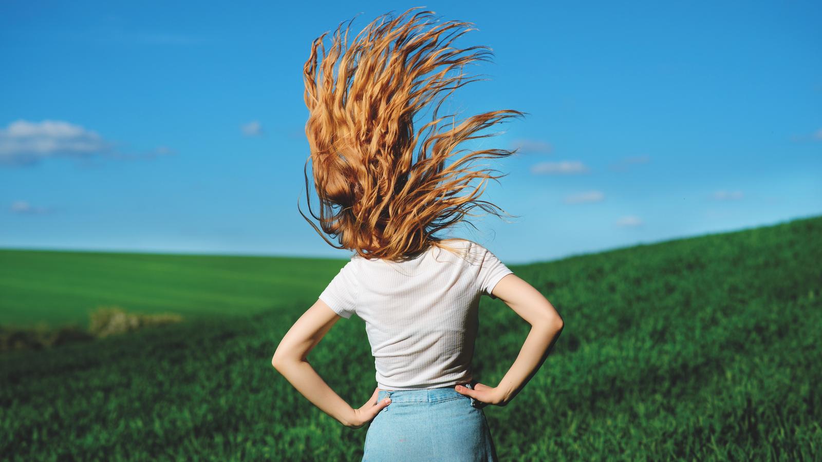 Frischer Wind in der Diabetologie Frau in Landschaft, Rücken zugekehrt mit wehende roten Haaren