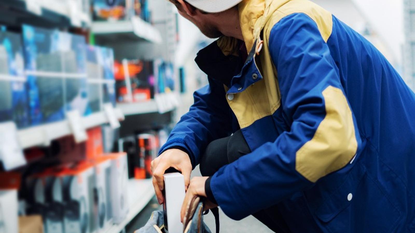 Junger Mann mit Kleptomanie steckt im Geschäft eine Verpackung in seinen Rucksack.