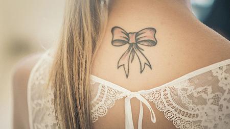 Rücken einer jungen Frau zeigt Tattoo einer Schlaufe