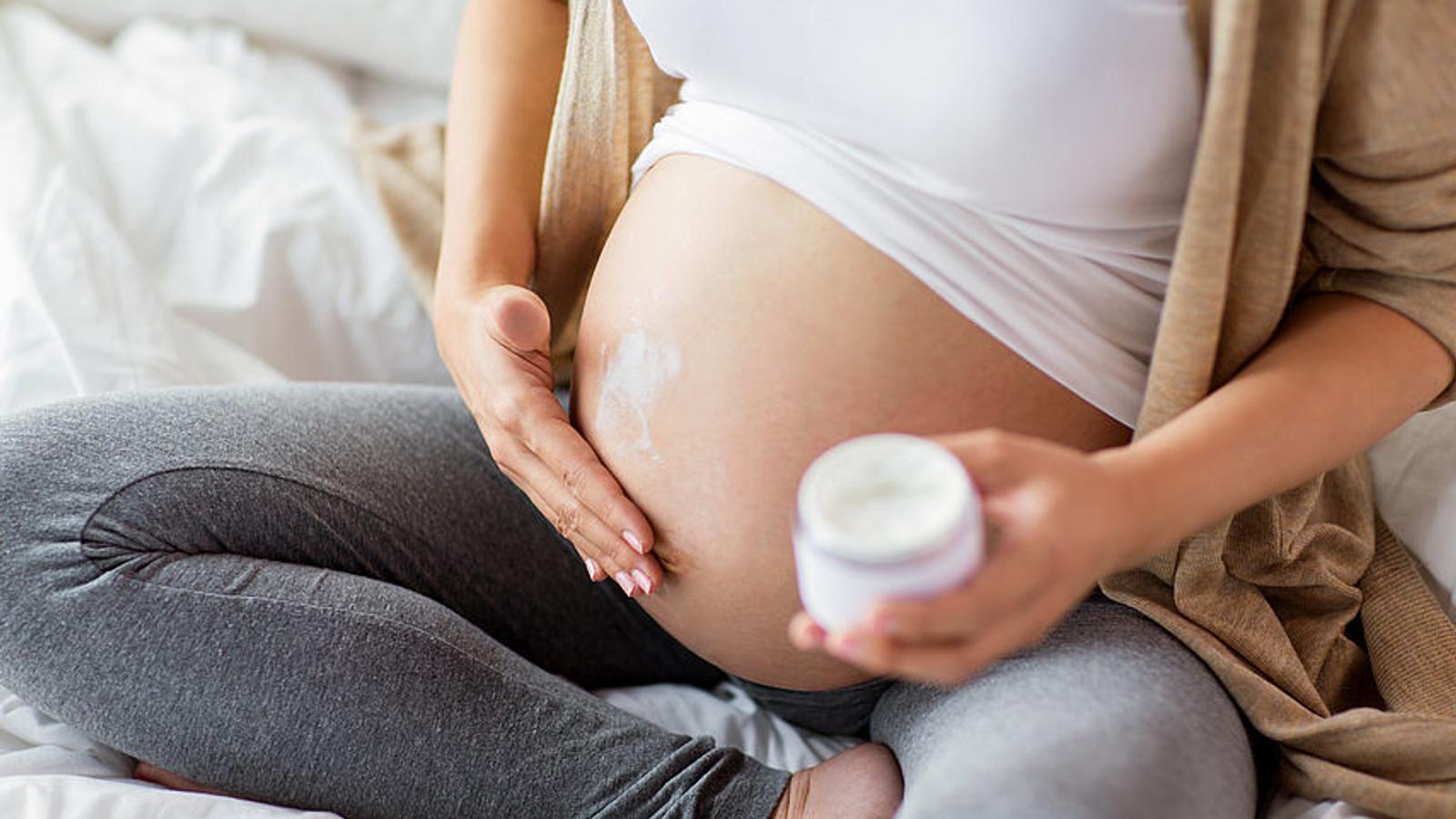 Schwangere Frau cremt sich ihren Bauch ein