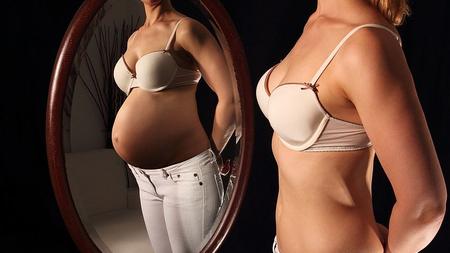 Frau steht vor dem Spiegel und stellt sich vor, sie wäre schwanger