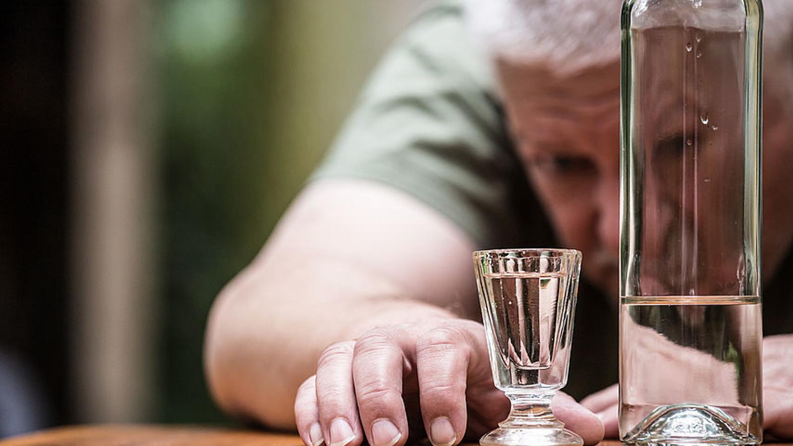 Vor einem Mann steht eine Schnapsflasche und ein Schnapsglas