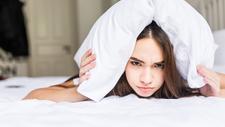 Frau mit Sex-Schmerzen liegt frustriert im Bett