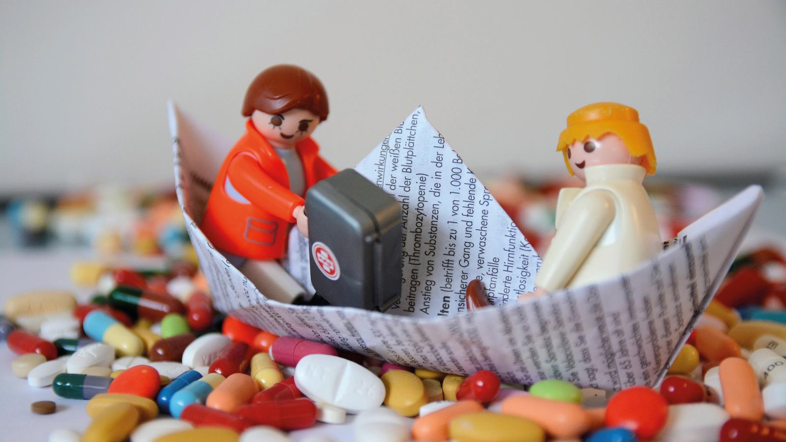 Playmobil-Arzt mit Arztkoffer und und Patient sitzen in einem Papierschiffchen