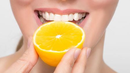 Frau isst Zitrusfrucht und gibt den Zähnen damit Saures