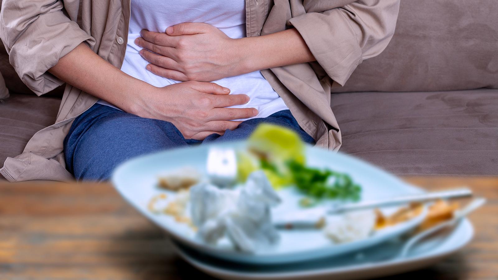 Frau ist nach dem Verzehr einer Mahlzeit übel und hält sich die Hände vor ihren Bauch