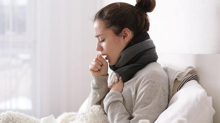 Frau liegt mit Grippe im Bett und hustet