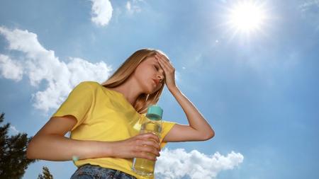 Frau mit einer Flasche Wasser, die unter einem Hitzschlag im Freien leidet