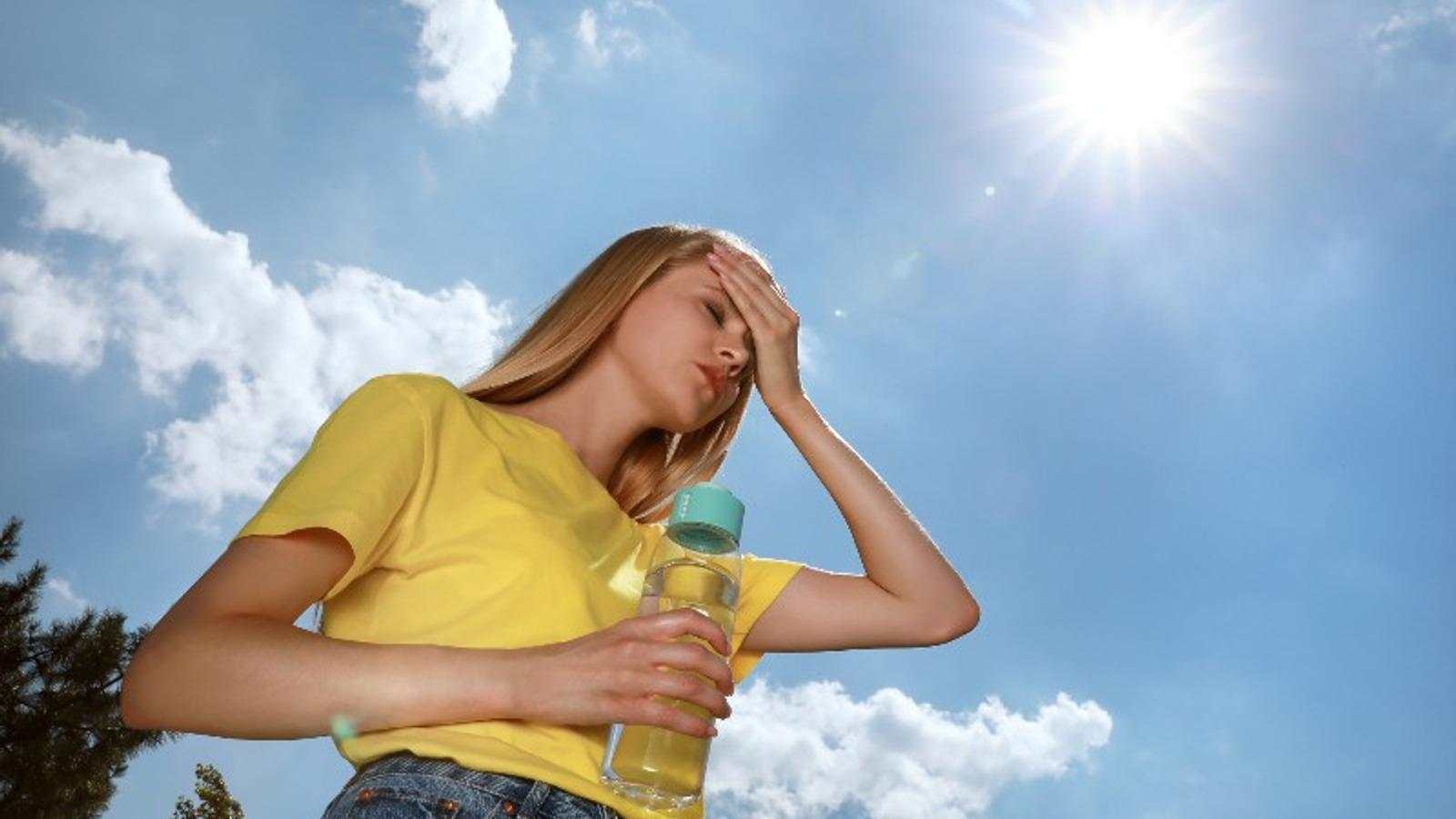 Frau mit einer Flasche Wasser, die unter einem Hitzschlag im Freien leidet