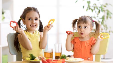 Zwei Mädchen finden gesunde Ernährung super und halten Paprika hoch