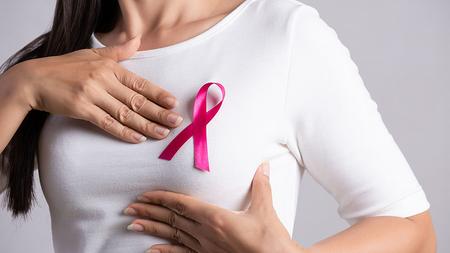 Frau mit pink Ribbon tastet ihre Brust ab. 